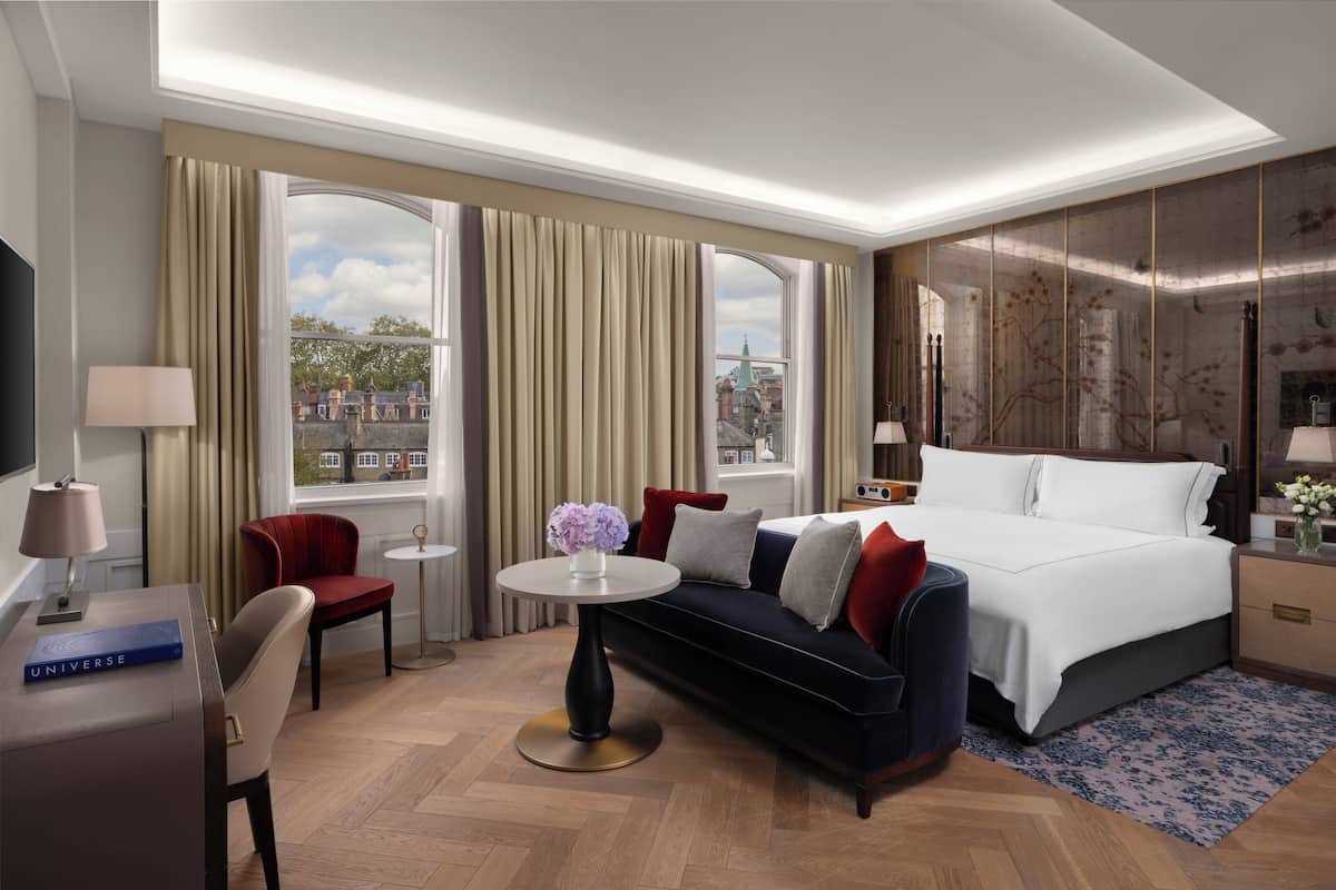 A modern hotel room with a large bed, a sofa, a desk, and a view of the city.