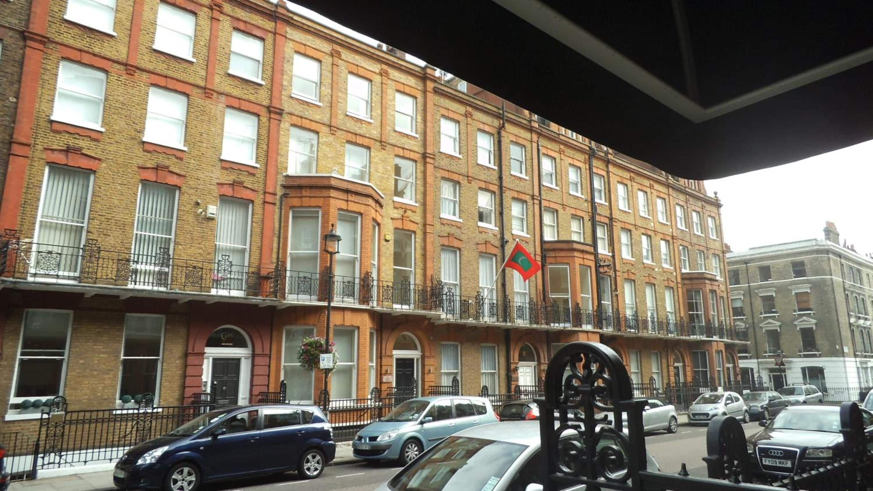 Un edificio residencial de varios pisos con fachada de ladrillo, múltiples ventanas y una bandera en la esquina.