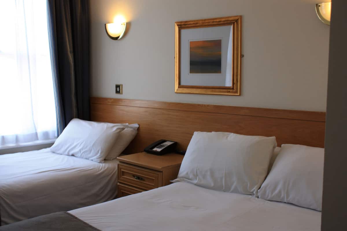 A hotel room with two beds, a nightstand, a phone, and a framed picture on the wall.