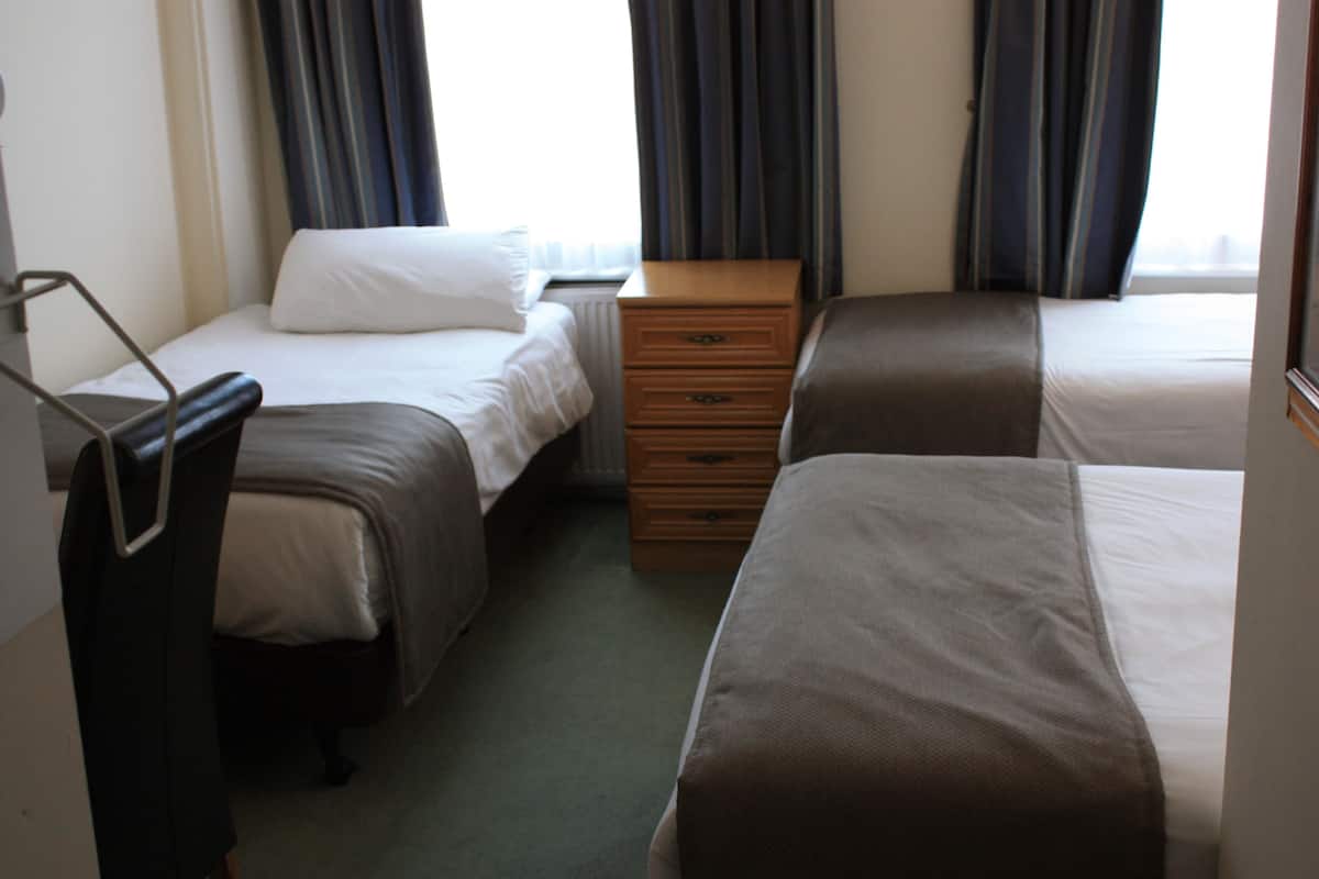 A hotel room with two single beds, a wooden dresser, and a chair.