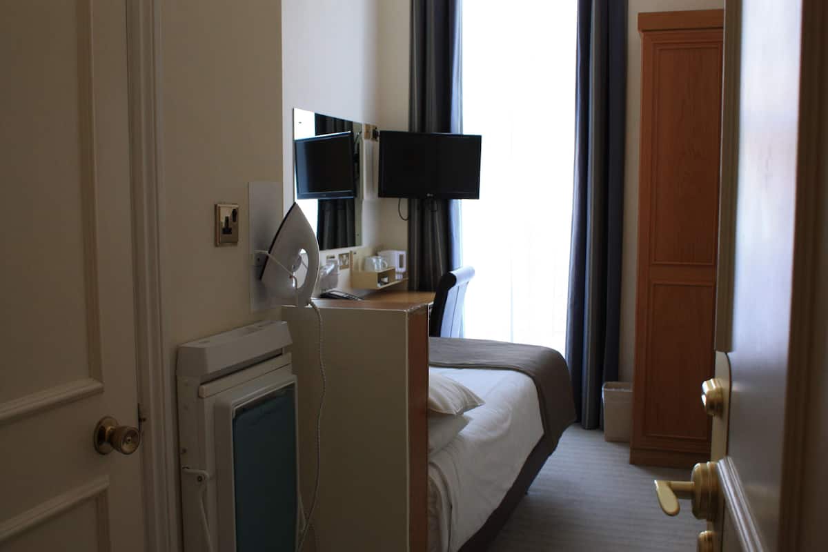 A hotel room with a bed, a desk with a computer and a monitor, a small kitchenette, and a door.