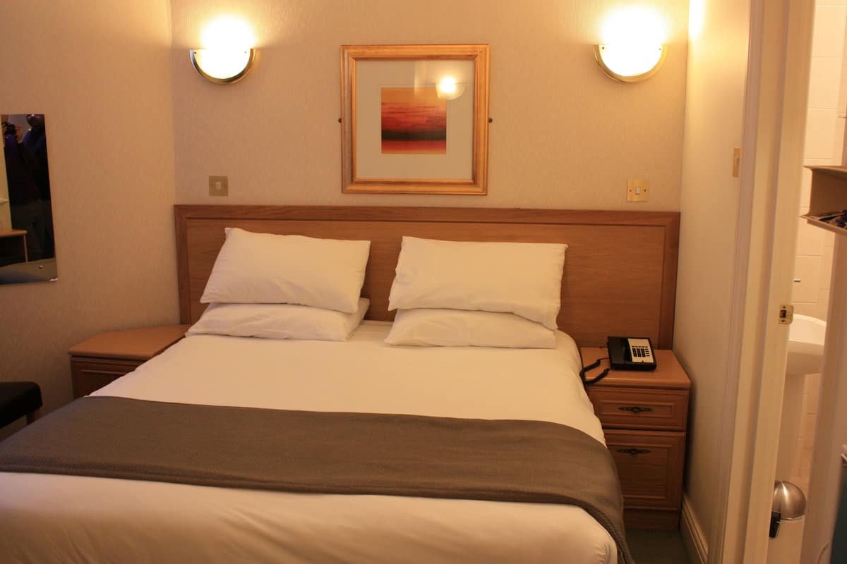 A hotel room with a bed, two bedside tables, a nightstand, a telephone, and a framed picture on the wall.