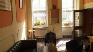 A room with a black leather sofa, a small stool, a chair, a vase, and a cabinet. - Gresham Hotel Bloomsbury (London)