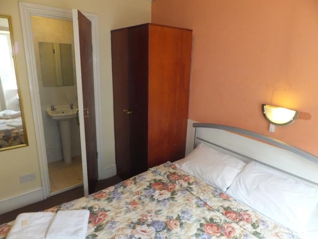 Quarto com cama, guarda-roupa, espelho e luminária na parede.