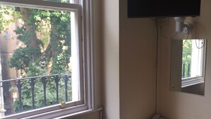 A room with a window, a television mounted on the wall, a desk with a telephone, and a trash bin. - Gresham Hotel Bloomsbury (London)