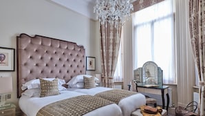 A spacious bedroom with a large bed, a wooden bench, a vanity with a mirror, and a chandelier.