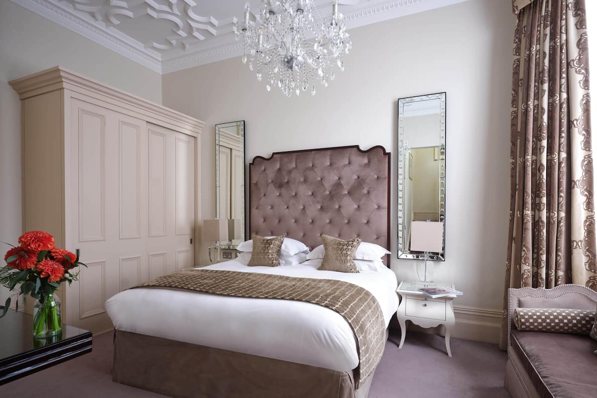 A spacious bedroom with a large bed, a chandelier, a vanity with a mirror, and a seating area with a chair.