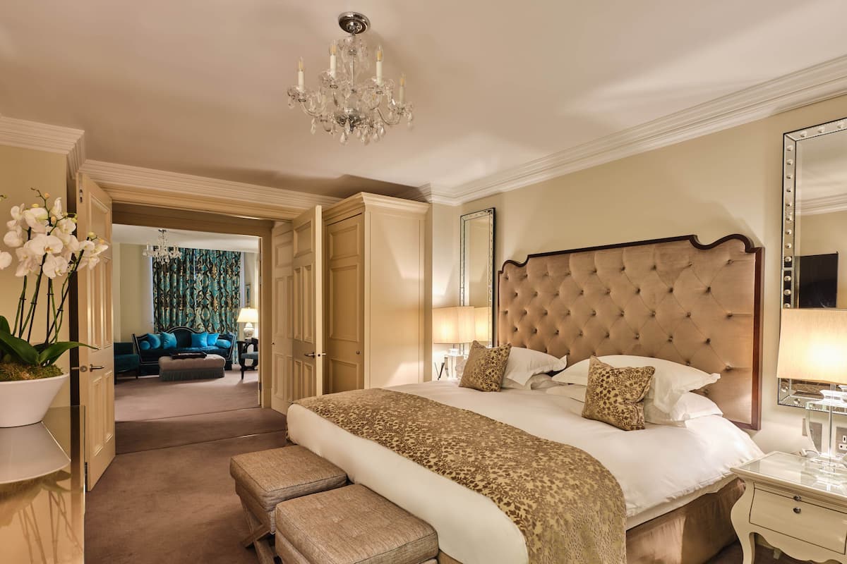 A spacious bedroom with a large bed, a chandelier, a sitting area with a sofa, and a mirror.