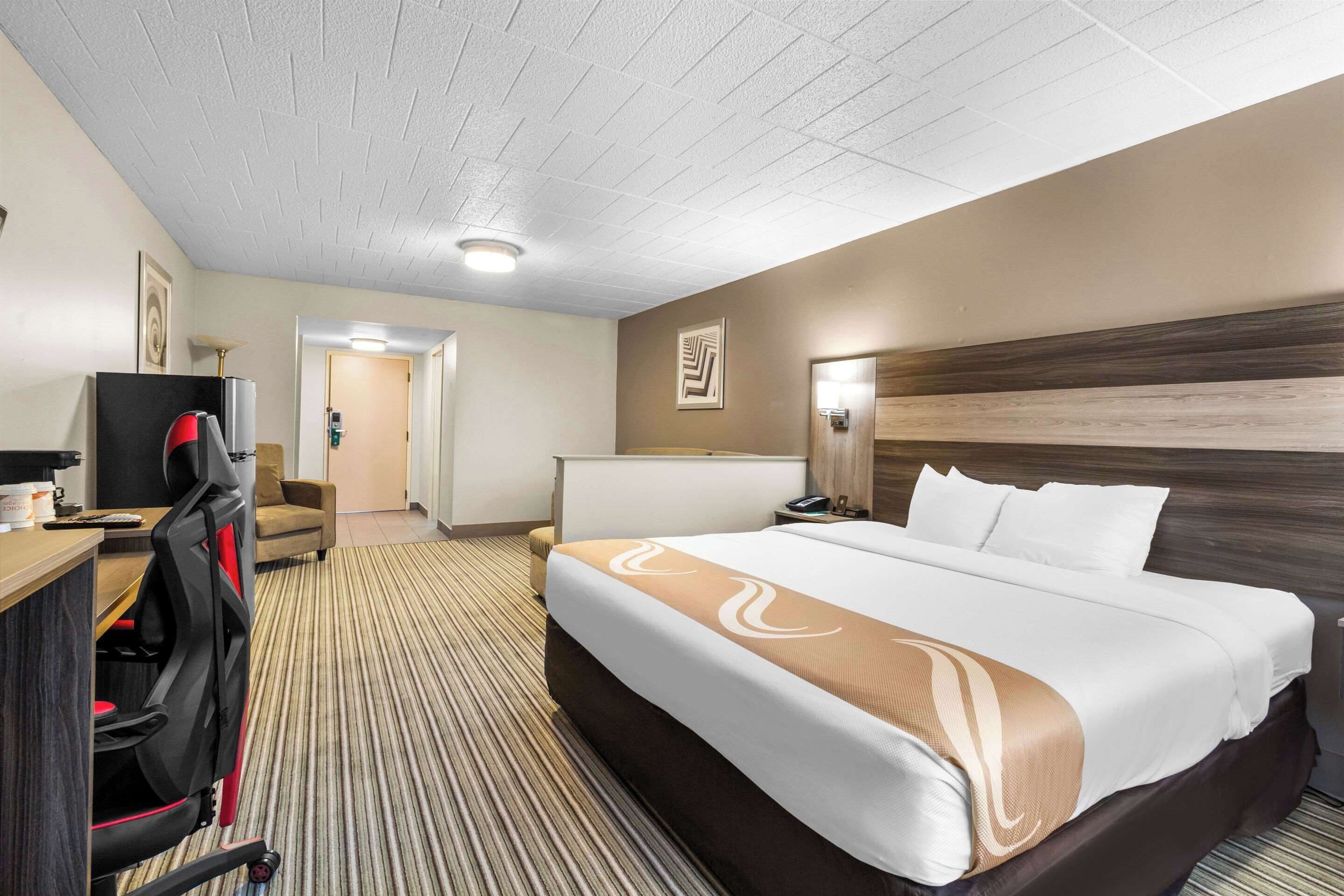 A hotel room with a large bed, a desk with a computer, a chair, and a television.