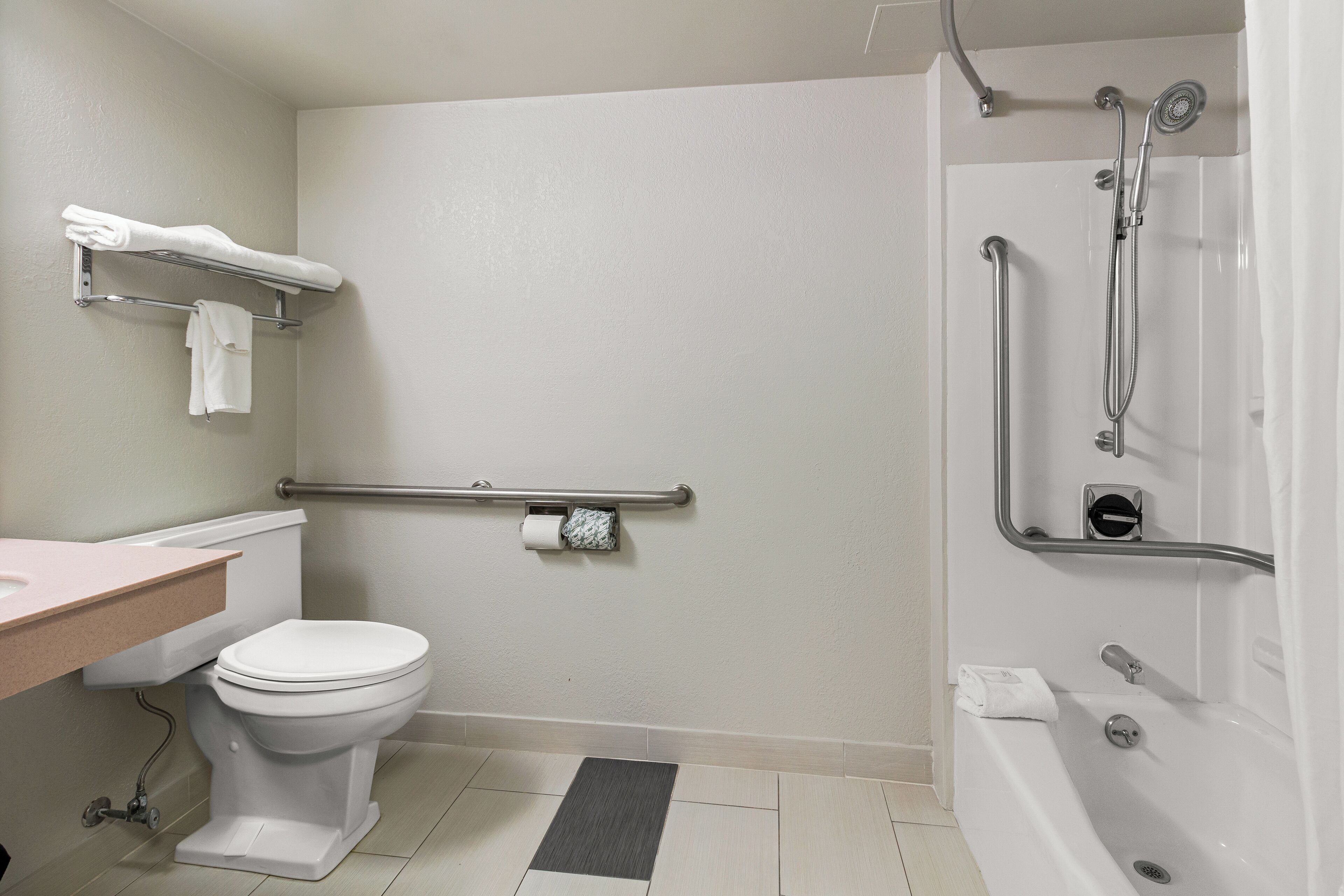 A bathroom with a toilet, sink, and bathtub. There is a grab bar next to the toilet and a showerhead above the bathtub.