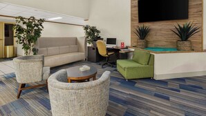 A modern lobby with a sofa, chairs, a reception desk, and two potted plants.