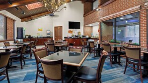 A spacious dining area with high ceilings, wooden beams, and a chandelier. Tables and chairs are arranged for dining.
