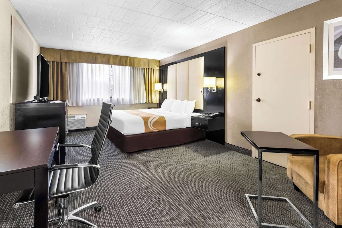 Ett hotellrum med en säng, ett skrivbord, en stol och ett litet bord.