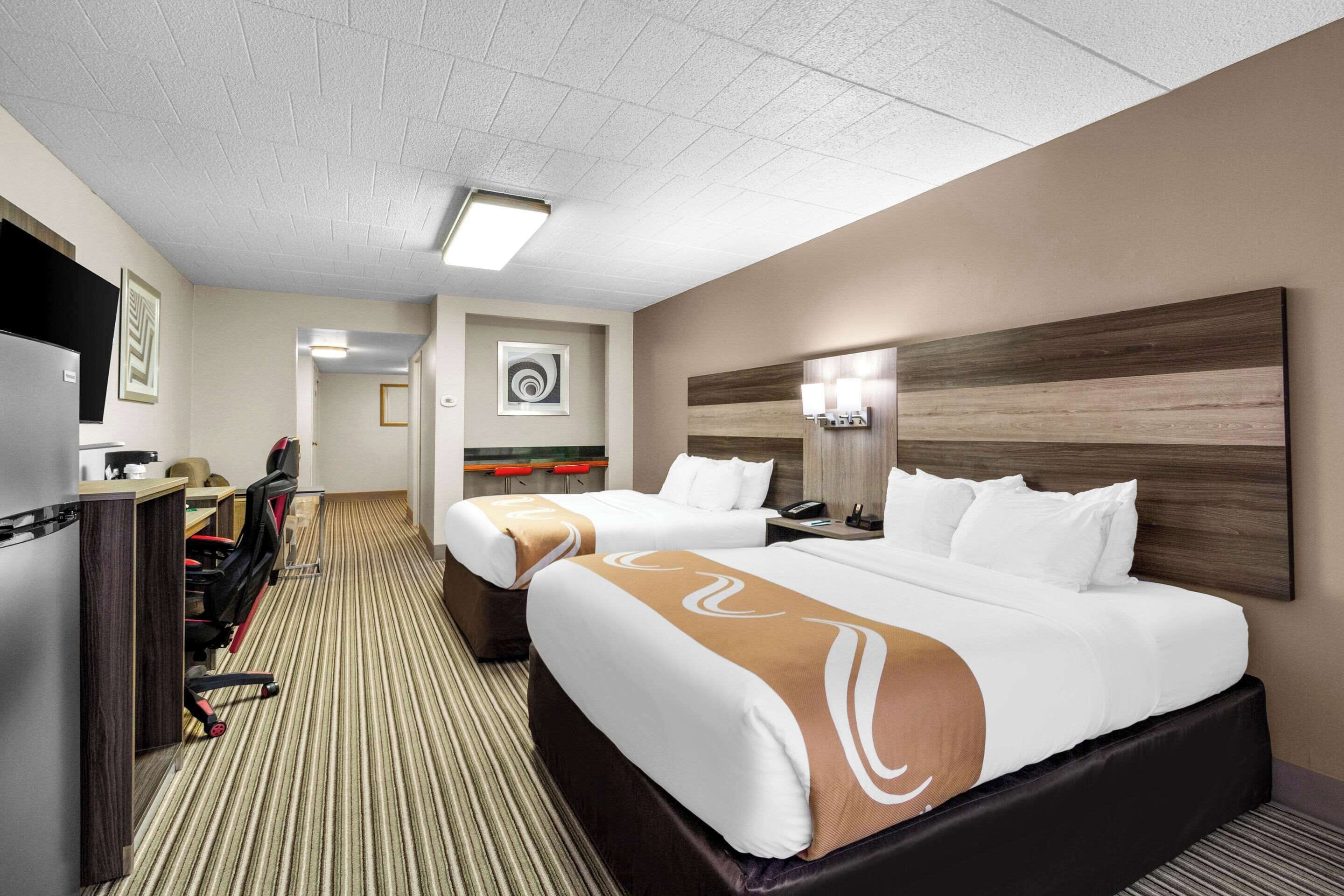 A hotel room with two beds, a desk with a chair, a TV, and a carpeted floor.