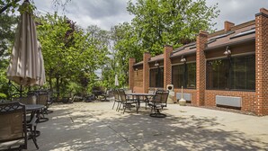An outdoor patio with tables and chairs, surrounded by brick buildings and trees.