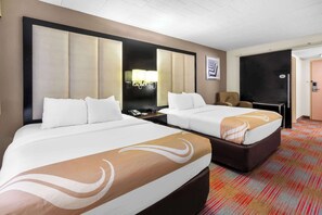 A hotel room with two beds, a desk, a chair, and a large mirror.