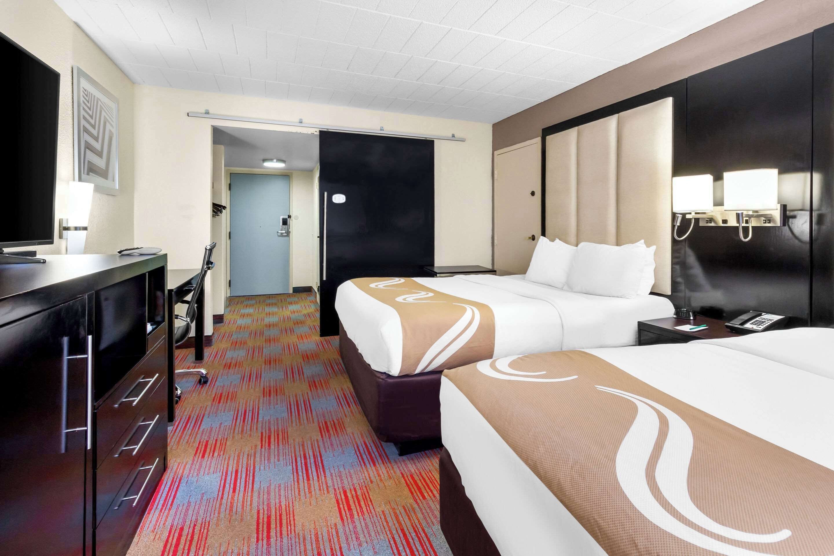 A hotel room with a large bed, a desk, a chair, and a television.