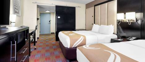 A hotel room with a large bed, a desk, a chair, and a television.