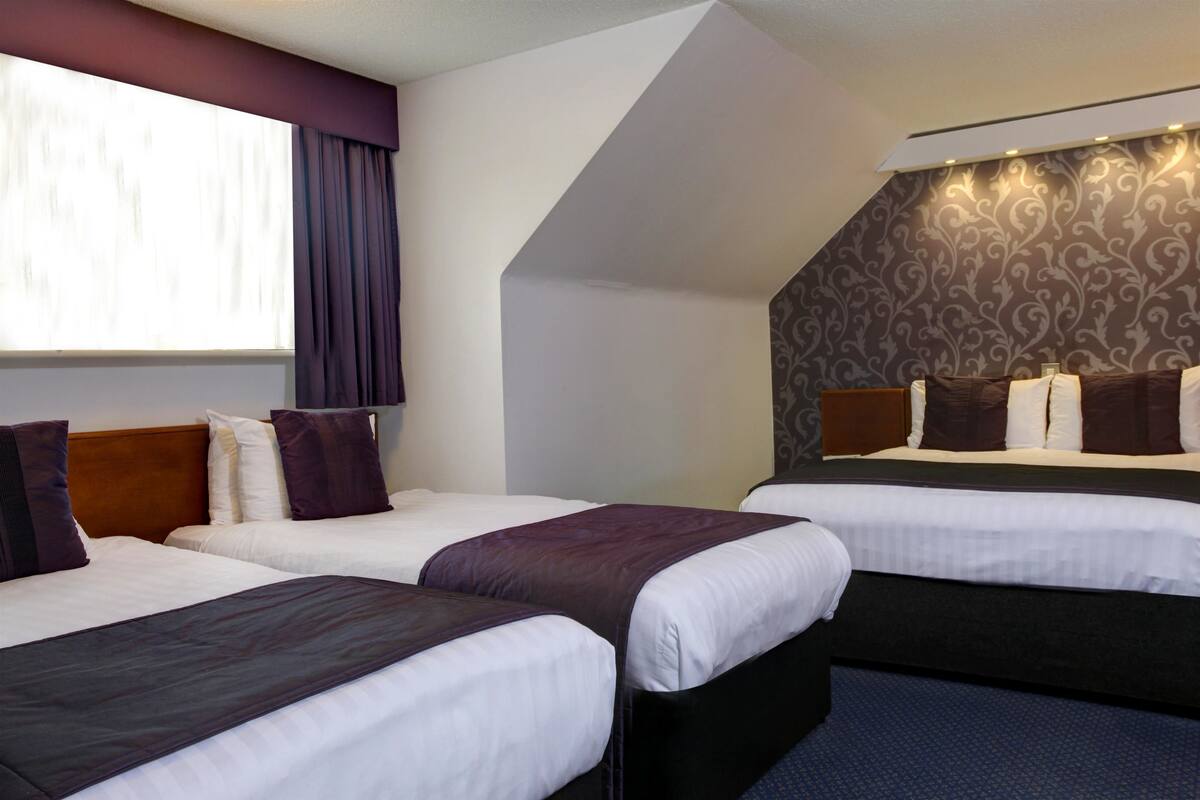 A hotel room with two beds, a large window with curtains, and a patterned wall.