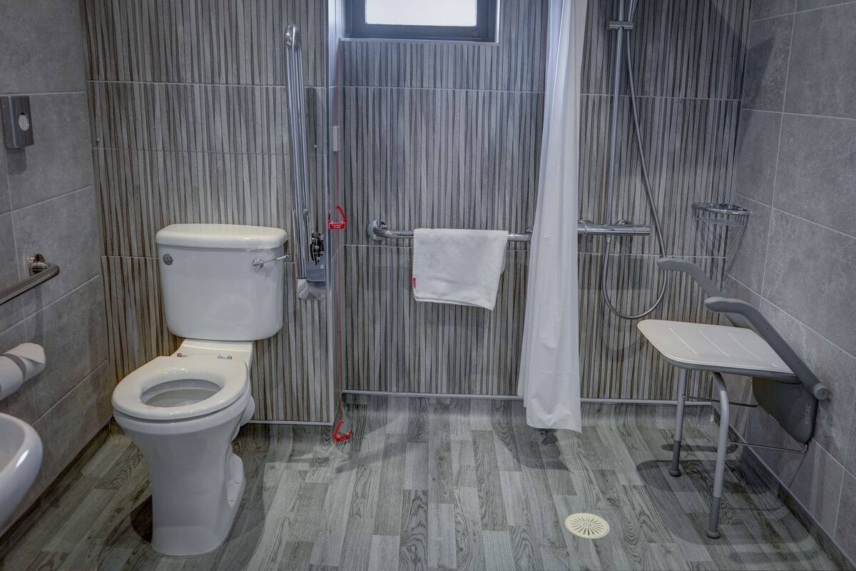 A modern bathroom with a toilet, shower, and grab bar.