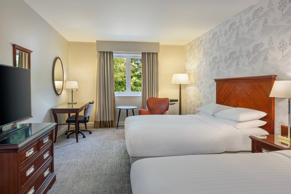 A hotel room with a large bed, a desk with a chair, a television, and a window with curtains.