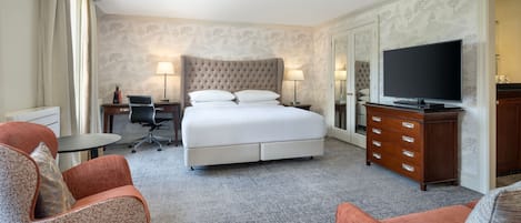 Une chambre d’hôtel avec un grand lit, deux tables de chevet, une télévision, un bureau et deux fauteuils.
