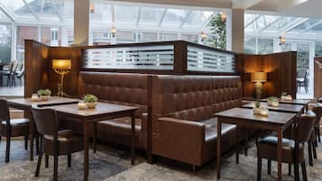 A modern dining area with leather booths, wooden tables, and potted plants.