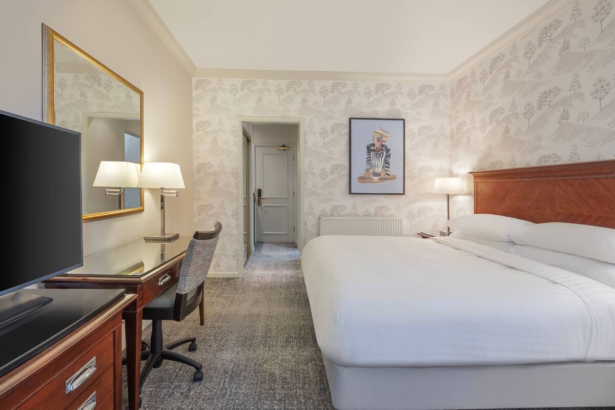 A hotel room with a bed, desk, chair, television, and a framed picture on the wall.