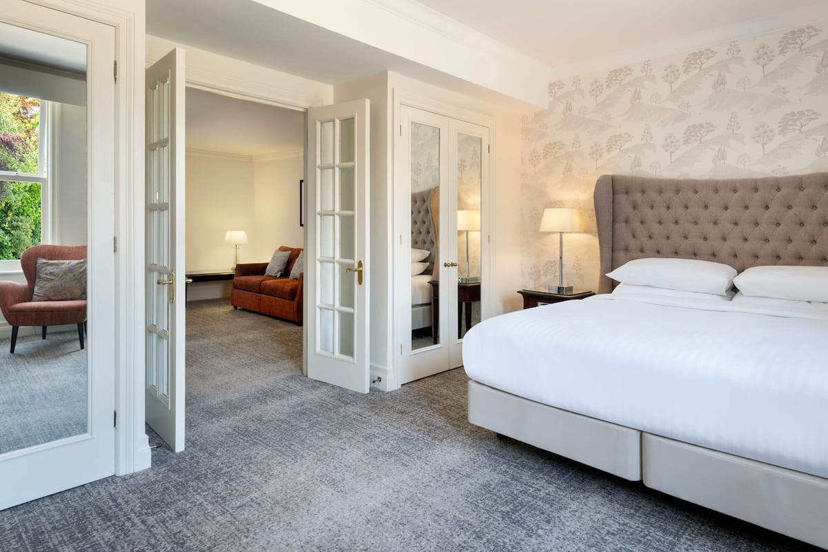 A hotel room with a large bed, a sitting area with a chair and a table, and a wardrobe with a mirror.