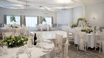 A banquet hall with round tables set for dining, chandeliers, and floral centerpieces.