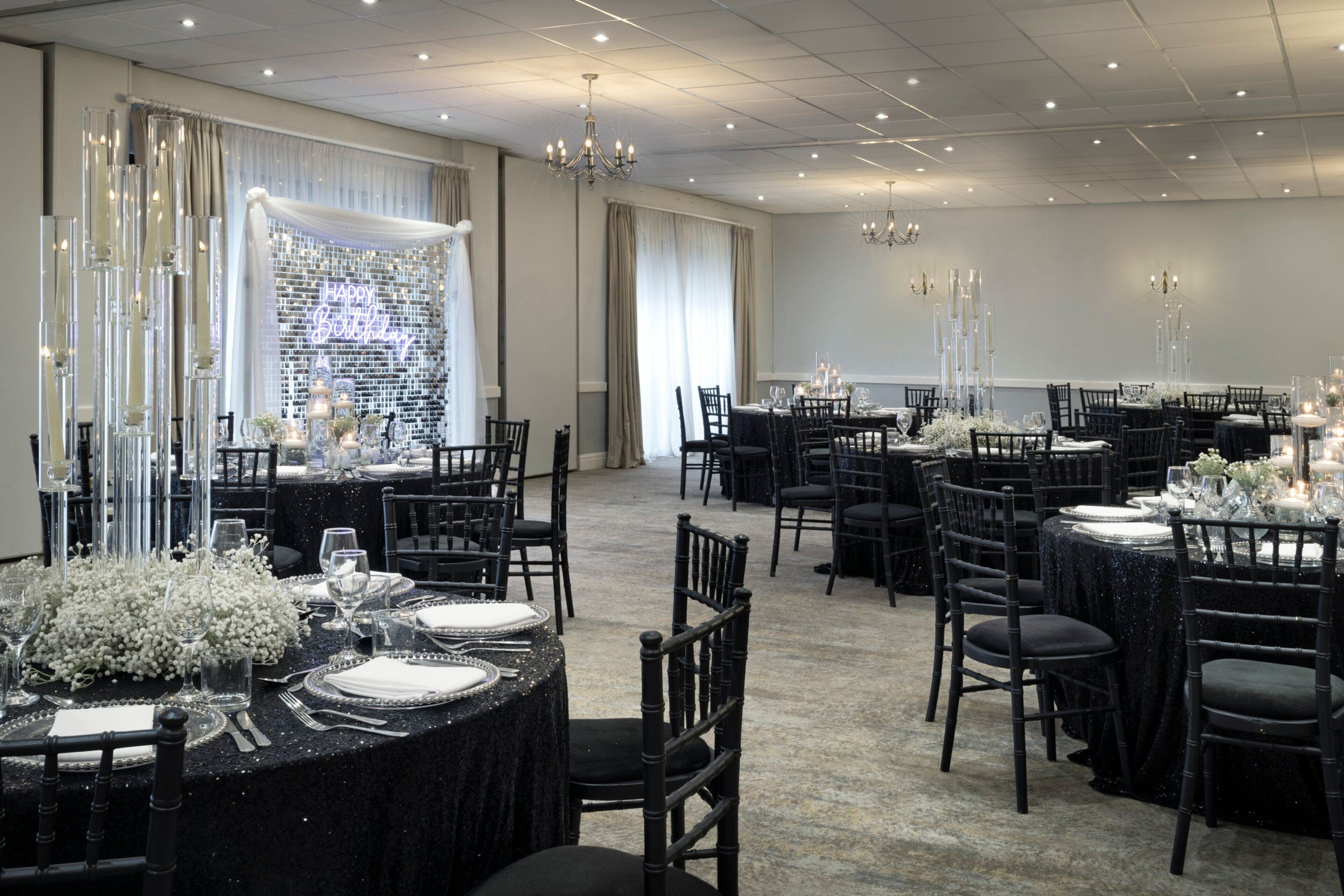 A banquet hall with round tables set for a formal event, featuring black tablecloths, white floral centerpieces, and tall candle holders.