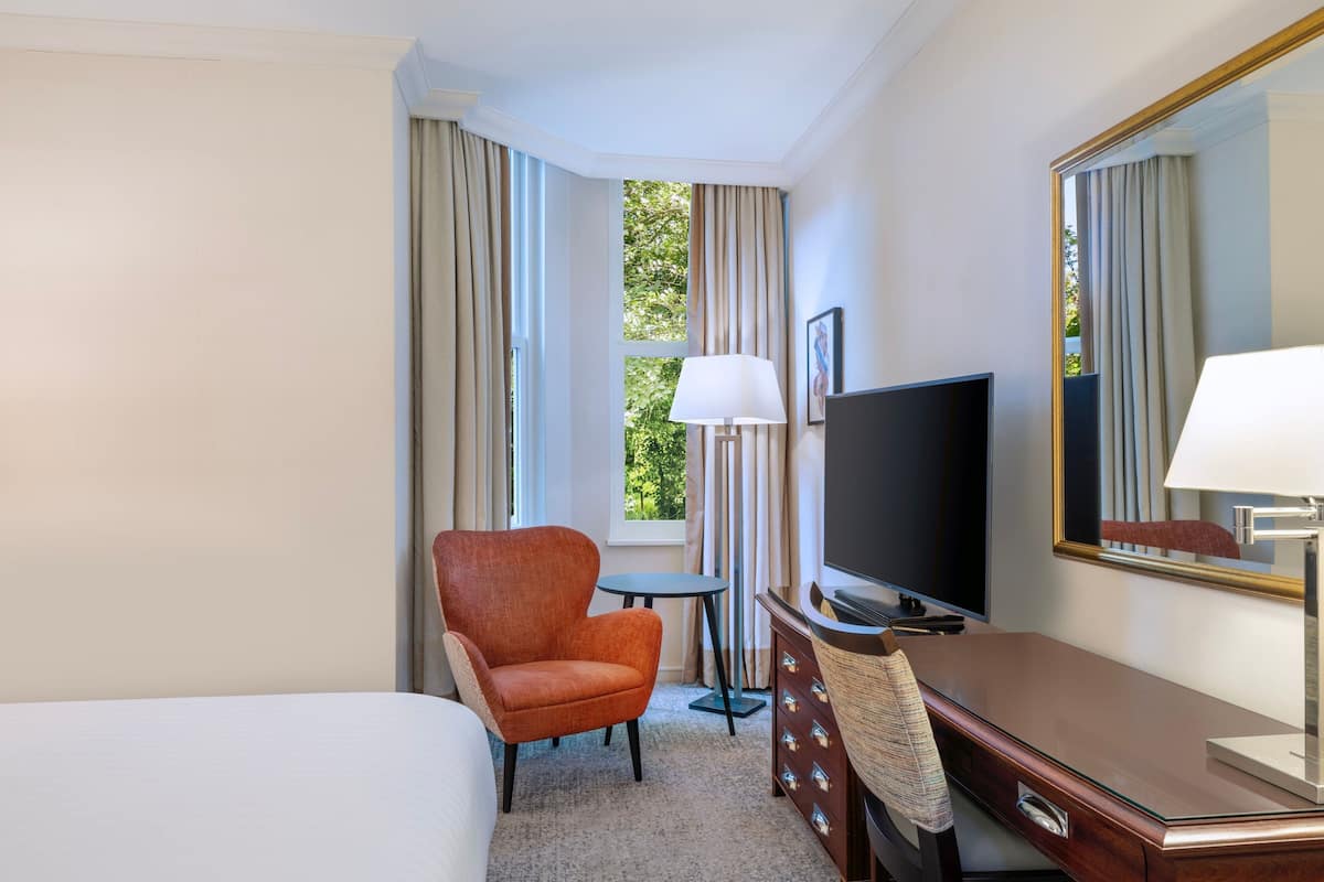 A hotel room with a bed, a TV, a chair, a small table, and a dresser.