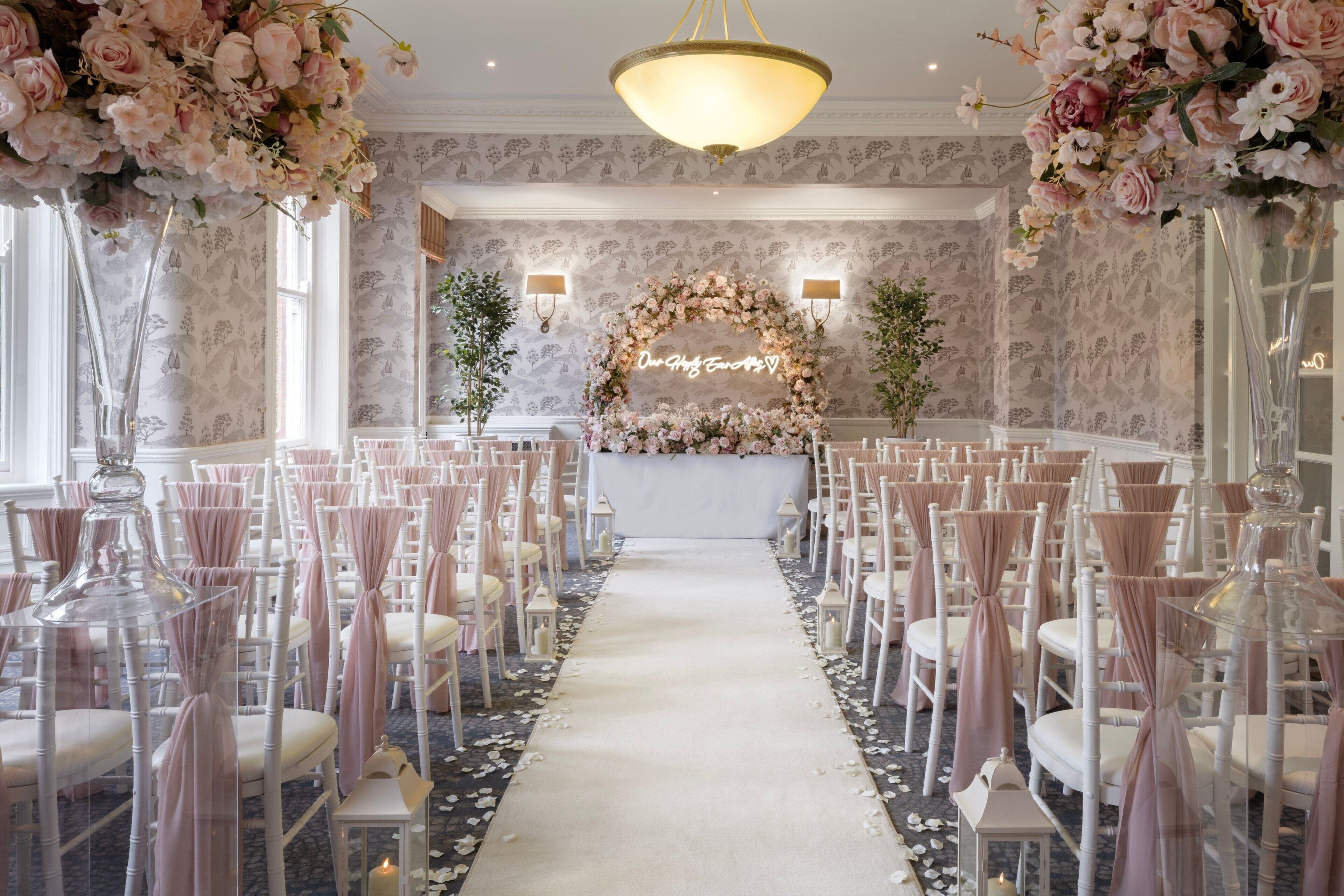 A wedding ceremony aisle with white chairs, a floral arch, and a chandelier.