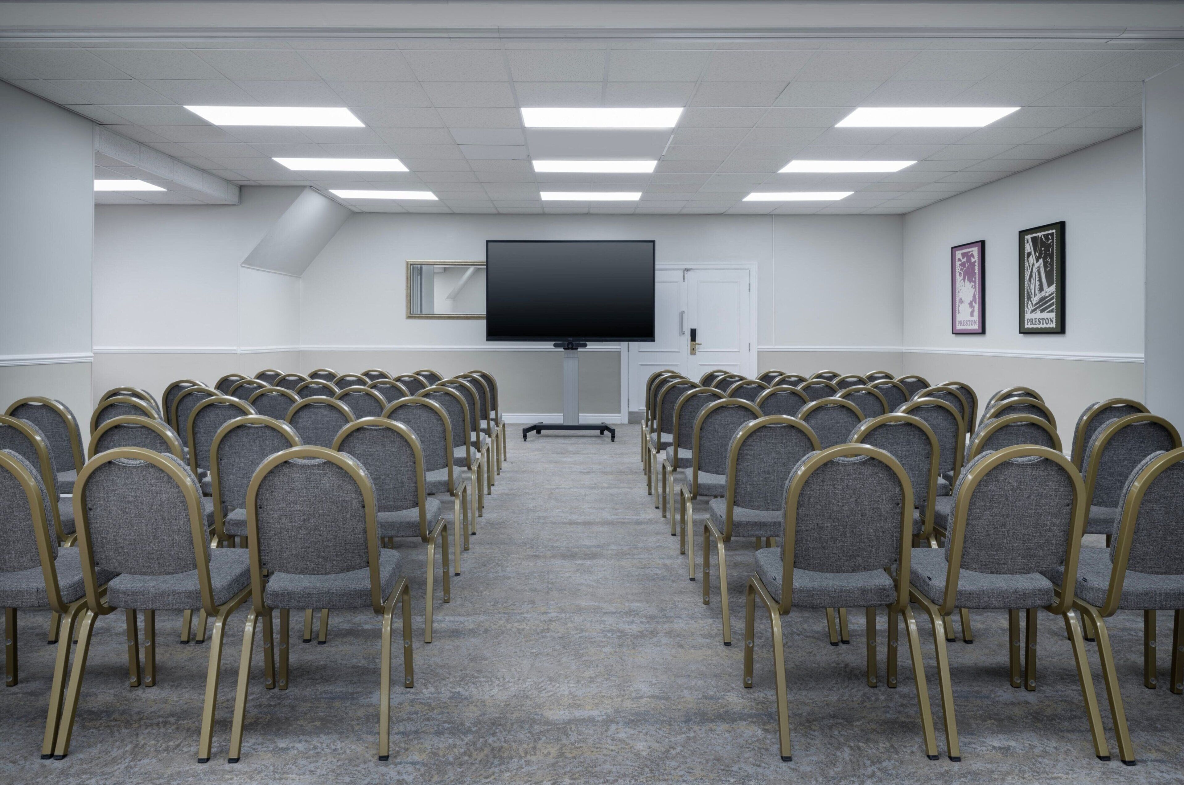 A conference room with rows of chairs, a large flat-screen TV, and framed pictures on the wall.
