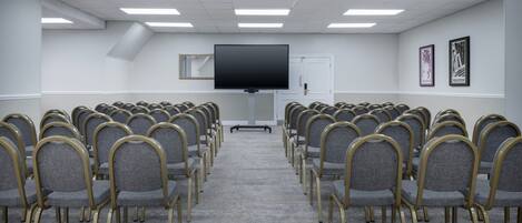 A conference room with rows of chairs, a large flat-screen TV, and framed pictures on the wall.