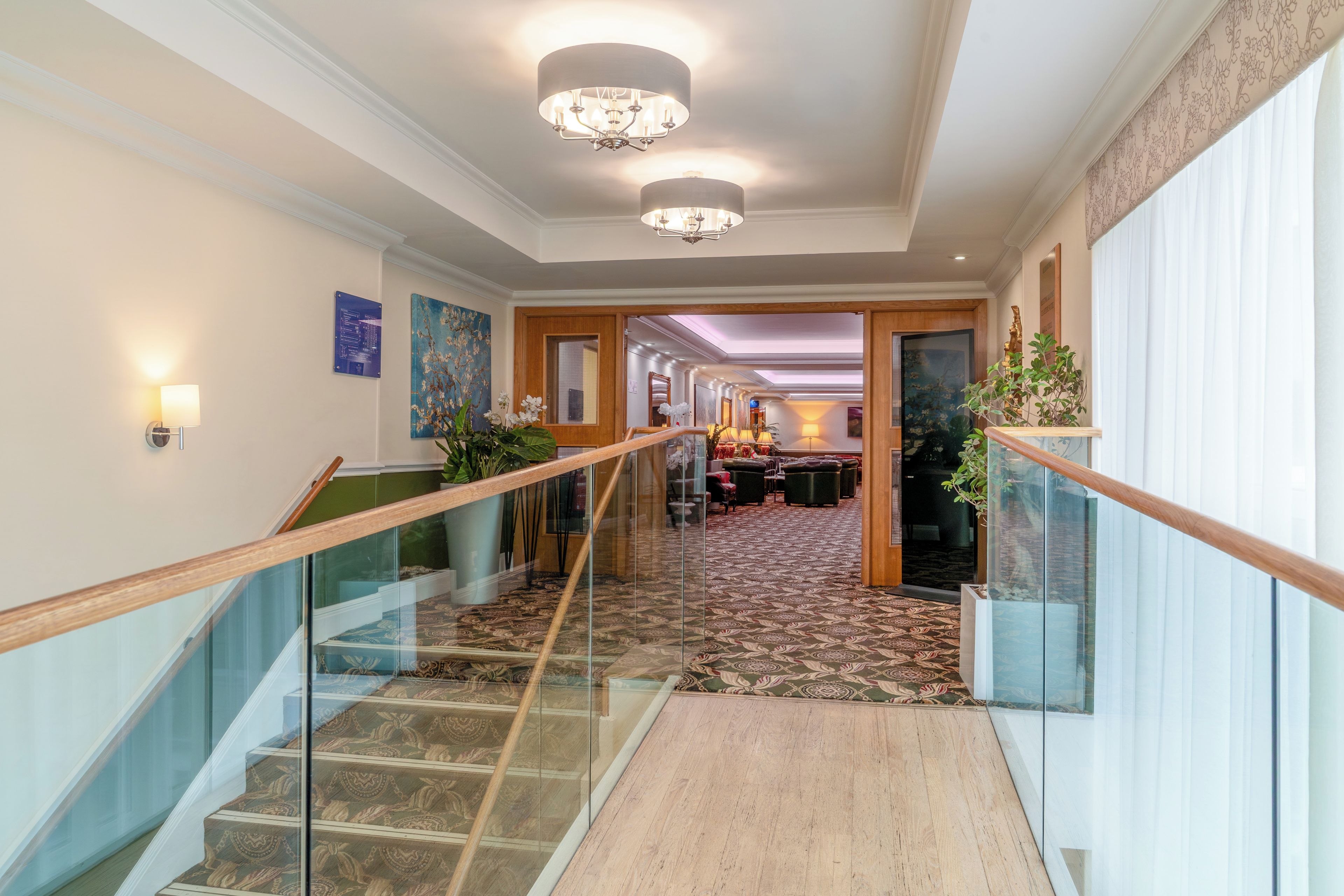A hotel hallway with a glass railing, patterned carpet, and a chandelier.