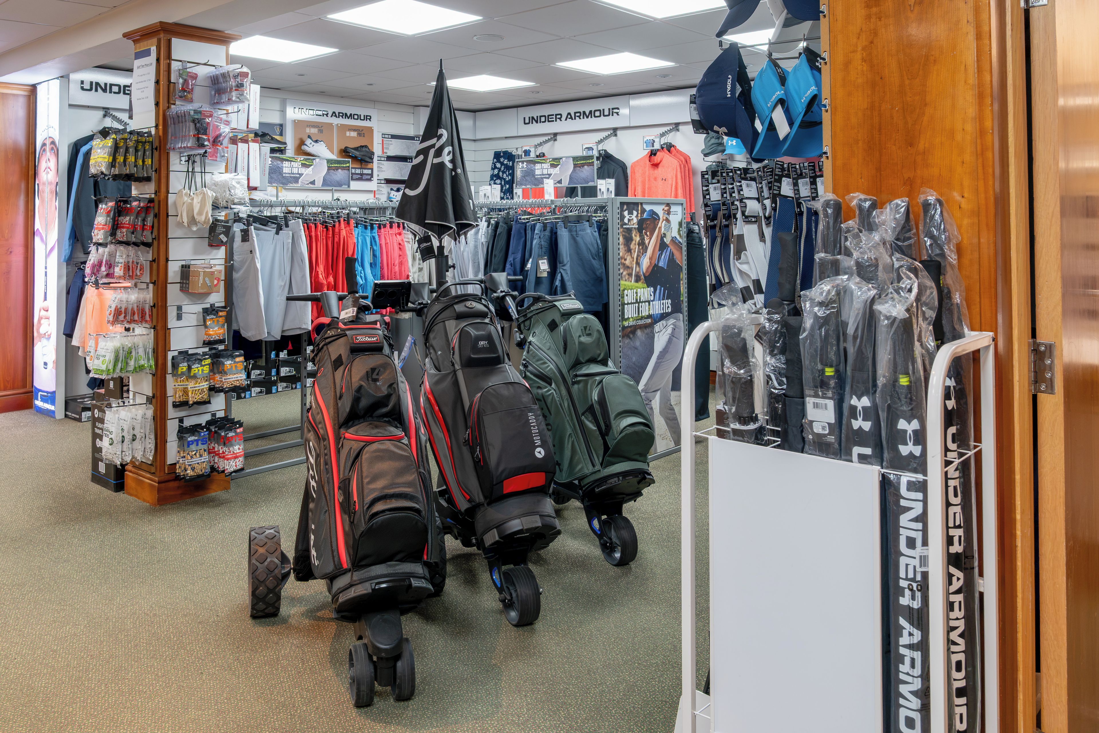 Un magasin de détail proposant divers articles et vêtements de sport, notamment des sacs de golf et des vêtements de la marque Under Armour.