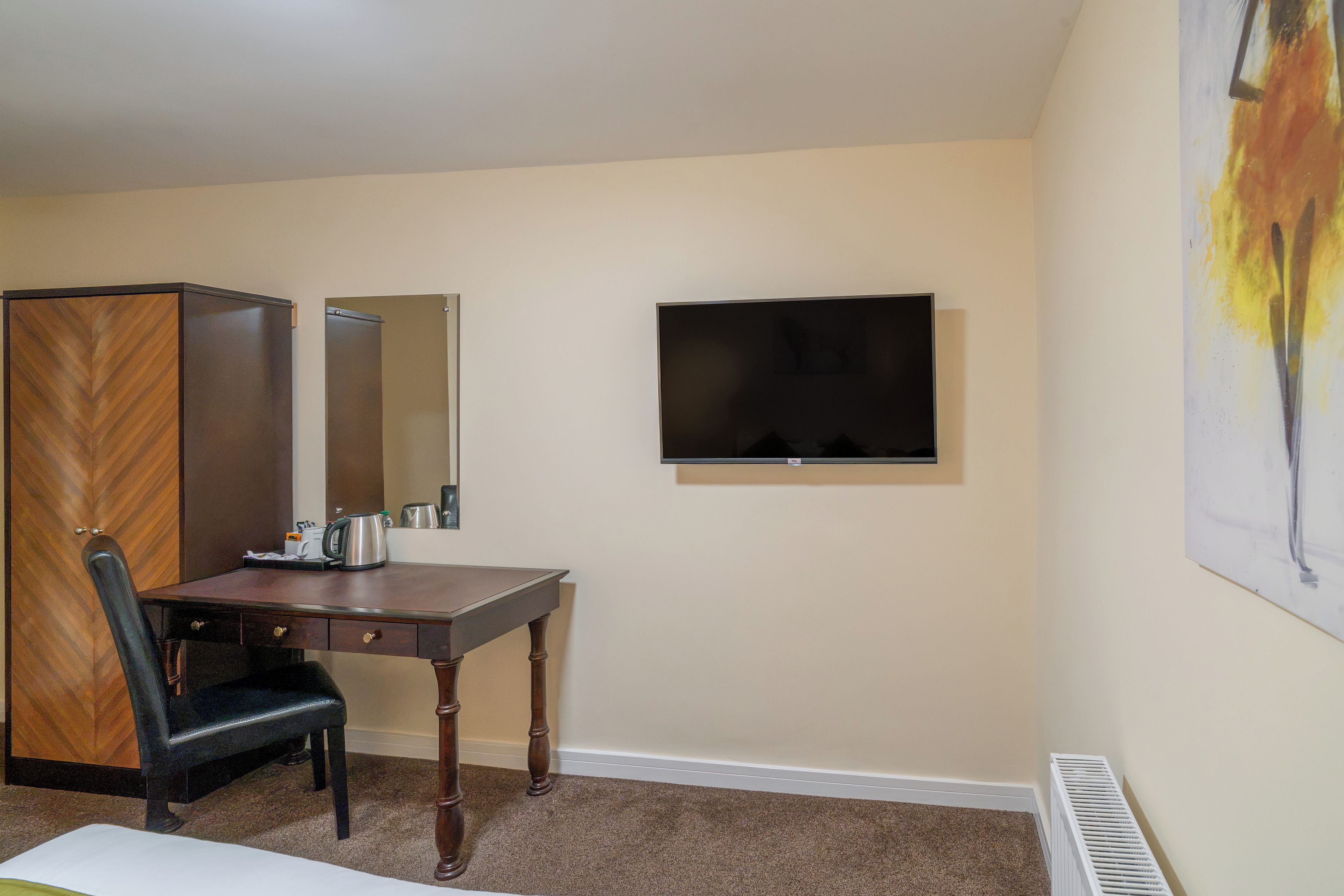 A hotel room with a desk, chair, wardrobe, flat-screen TV, and a radiator.