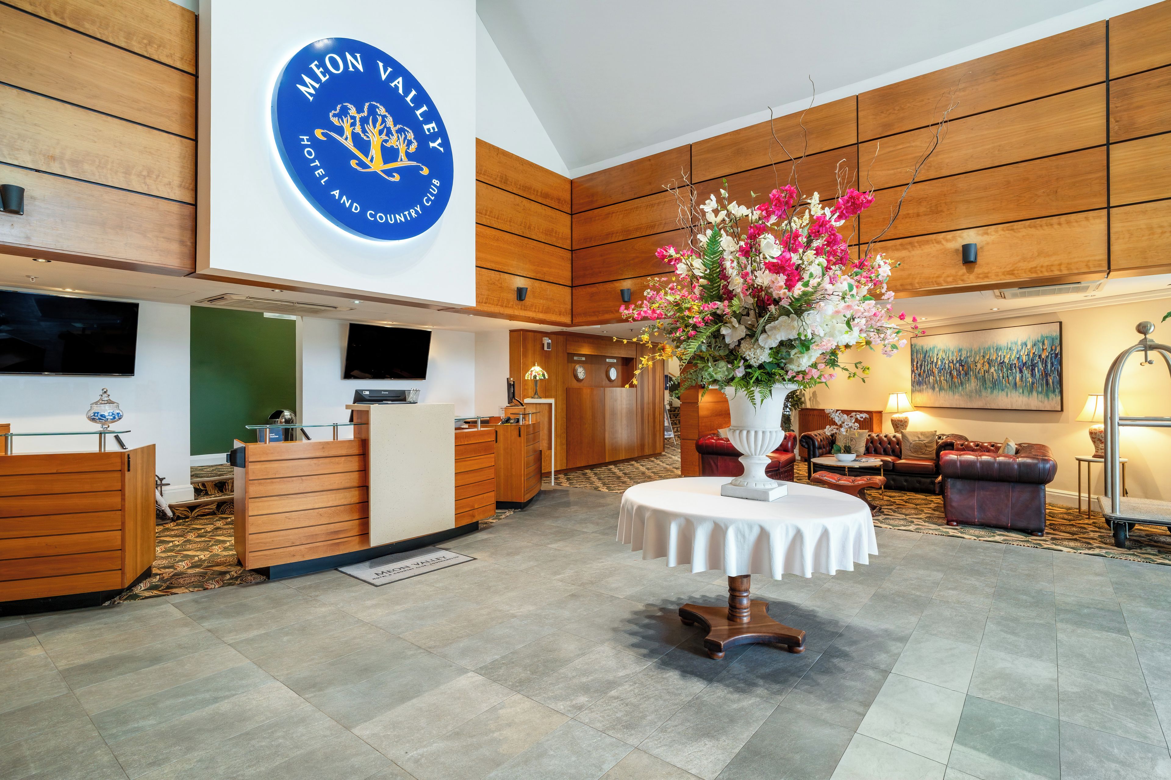 Vestíbulo de hotel con mostrador de recepción, un gran centro de flores y un área de descanso con sofás de cuero.