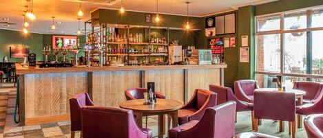 Zona de bar con mostrador de madera, estanterías con botellas y sillas moradas alrededor de una mesa central.