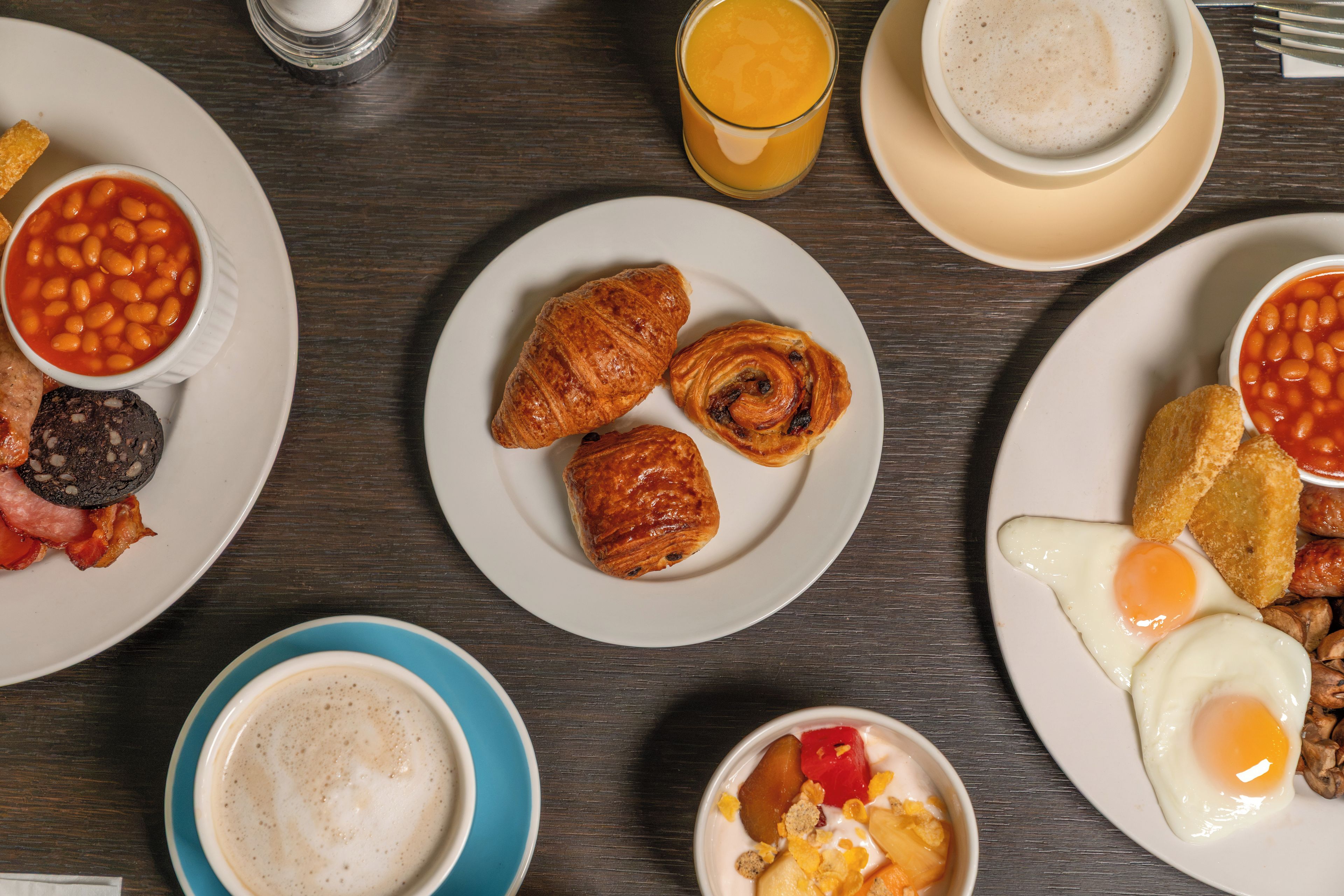 A breakfast table with plates of beans, croissants, eggs, and toast.