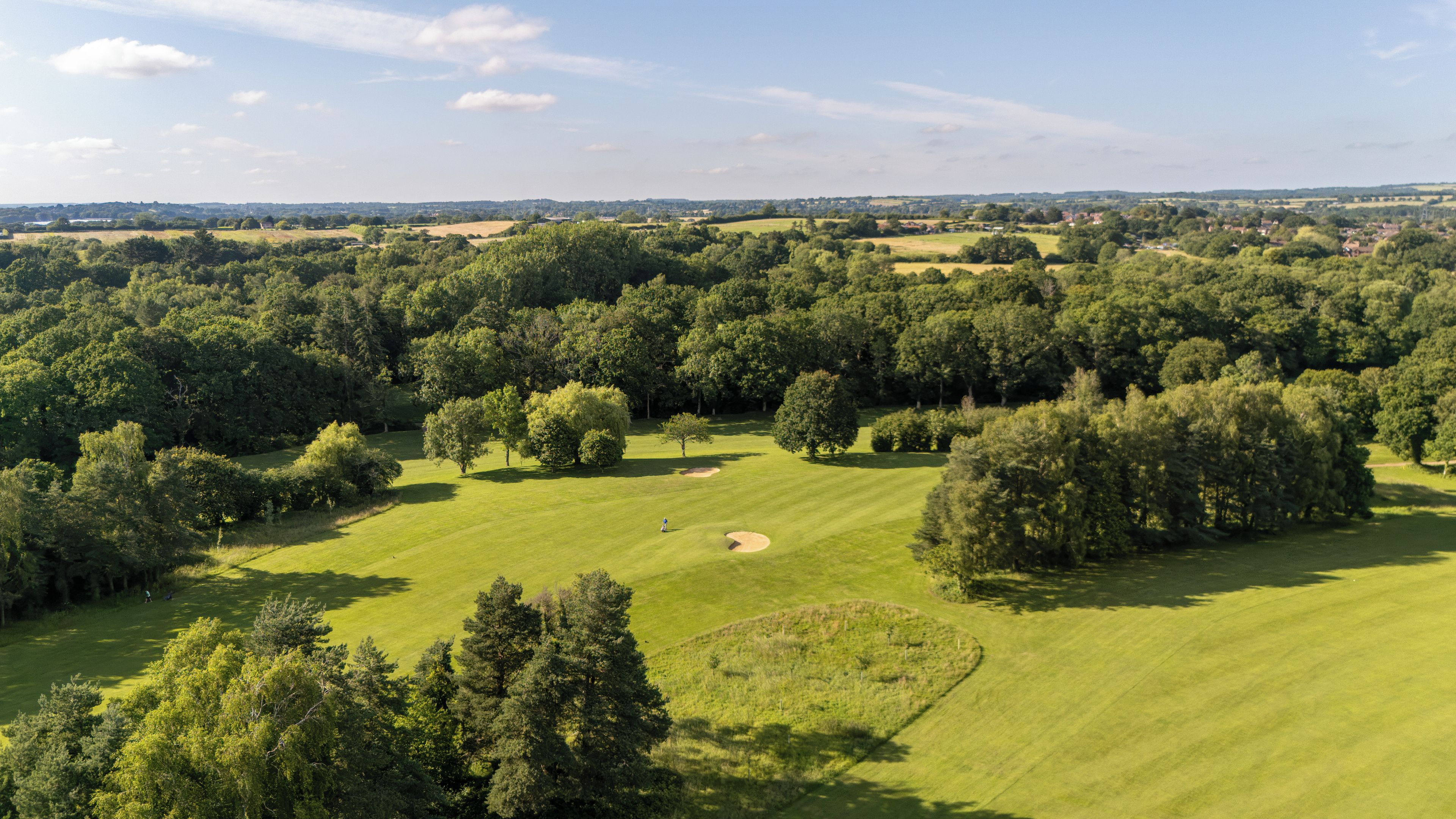 A golf course with multiple holes, surrounded by dense trees and open fields.
