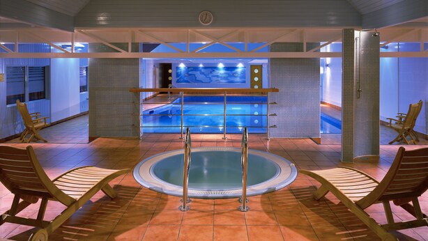 A pool area with a hot tub, lounge chairs, and a clock on the wall. - Meon Valley Hotel, Spa & Golf (Southampton)