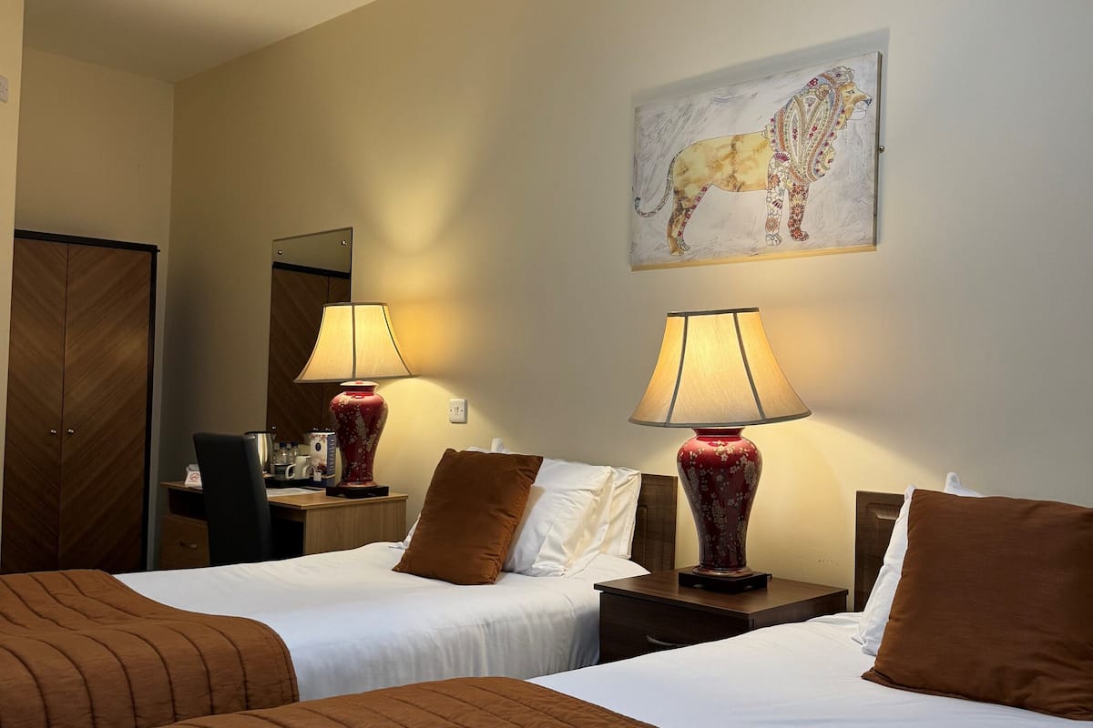 A hotel room with two beds, each with brown bedding, a red vase lamp, and a painting of a lion on the wall.
