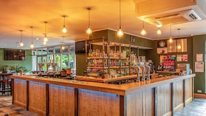 A bar area with a wooden counter, hanging light bulbs, and shelves stocked with bottles. - Meon Valley Hotel, Spa & Golf (Southampton)
