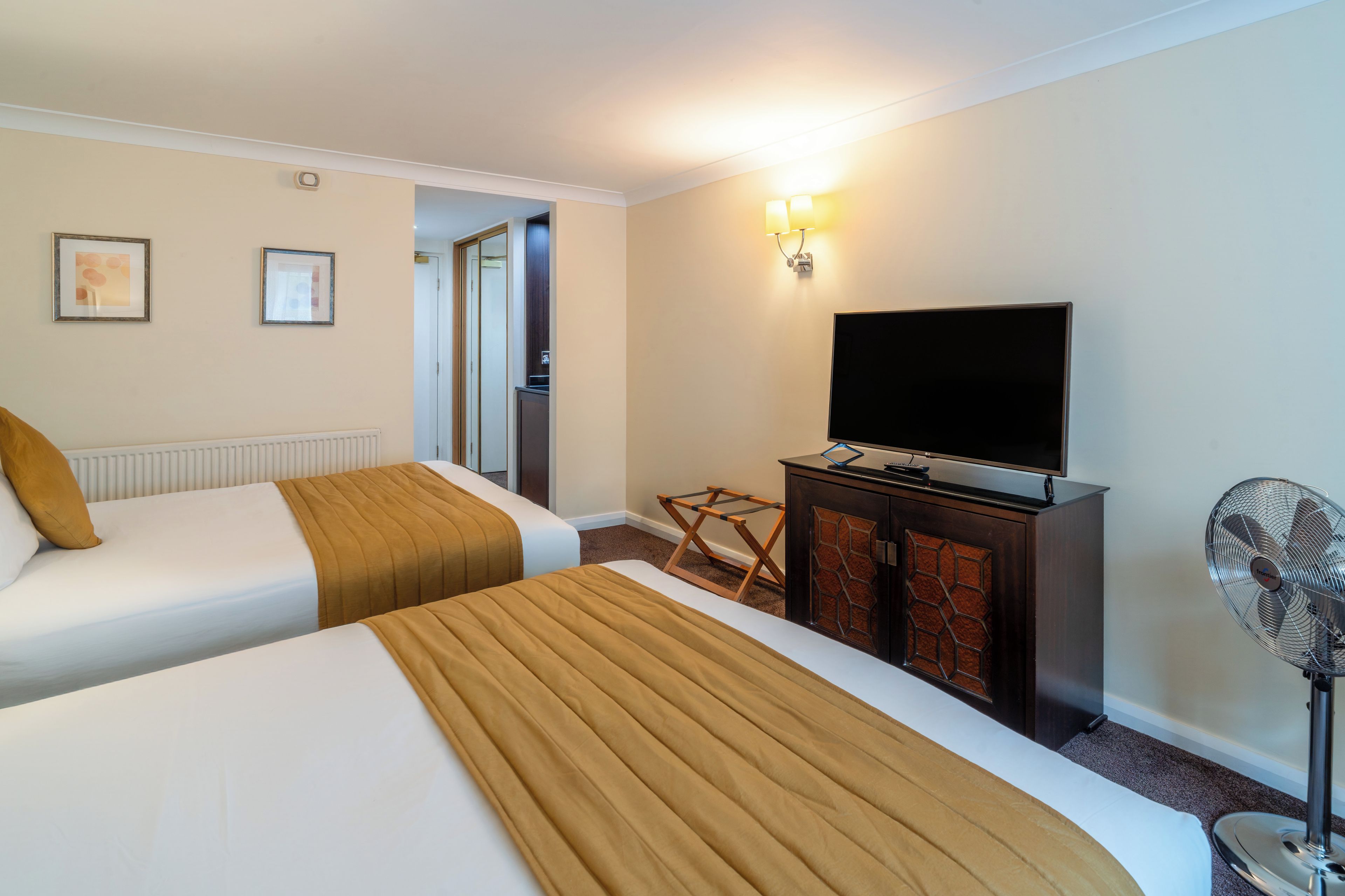 Camera d'albergo con due letti, una televisione, una scrivania con un computer, una ventola da pavimento e una porta che dà su un bagno.