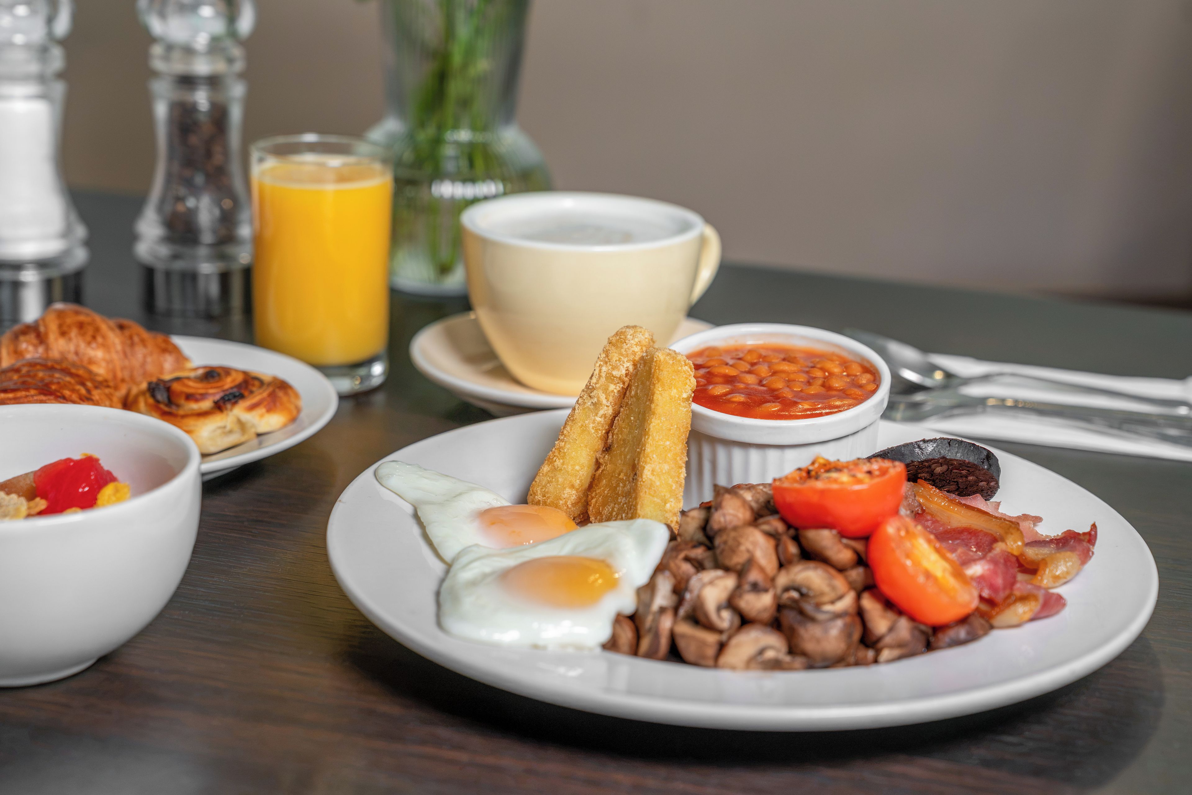 A breakfast plate with eggs, mushrooms, tomatoes, bacon, and beans.