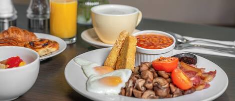 A breakfast plate with eggs, mushrooms, tomatoes, bacon, and beans.