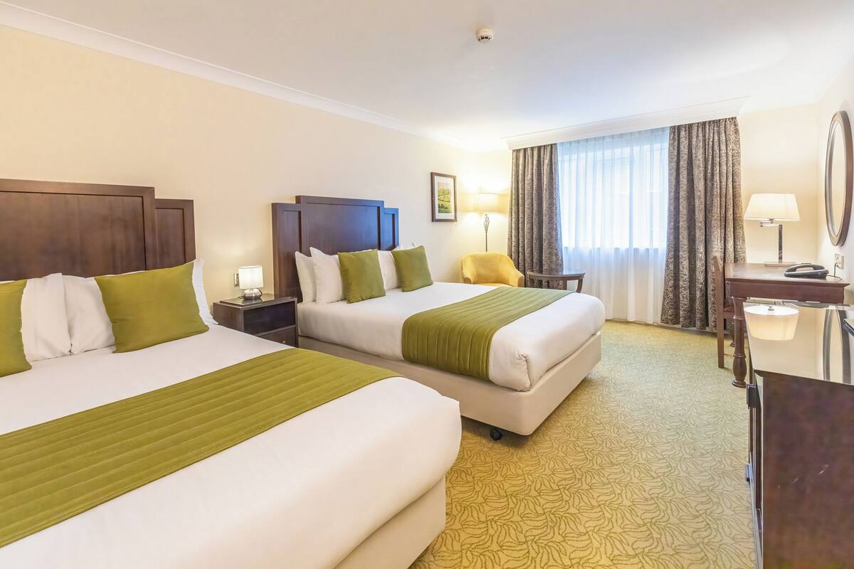 A hotel room with two beds, a desk, a chair, a lamp, and a mirror.