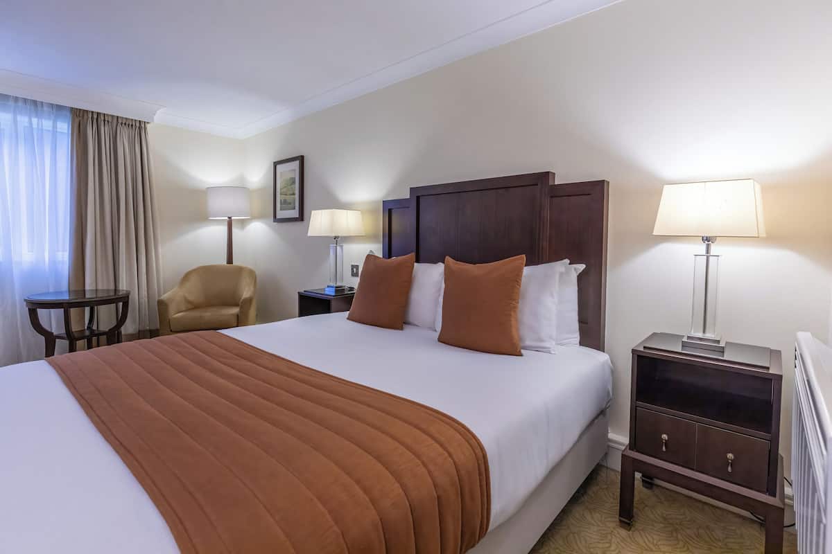 A hotel room with a large bed, two bedside tables with lamps, a chair, and a small table.